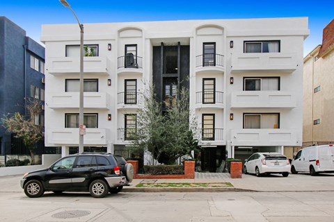 A black SUV is parked in front of a white building with a tree in front of the building.