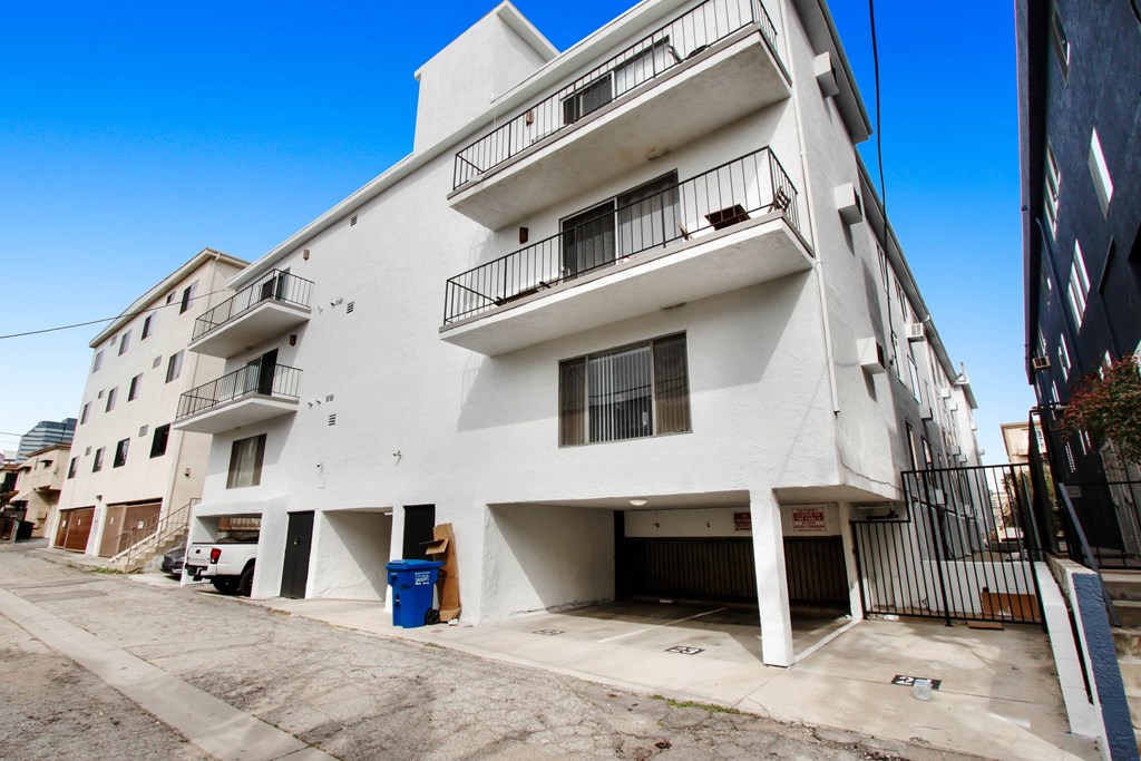 A white building with balconies and a blue trash bin in front.