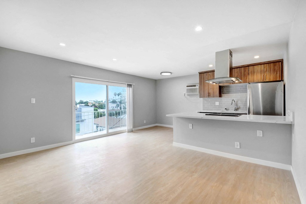an empty living room with a kitchen and a sliding glass door