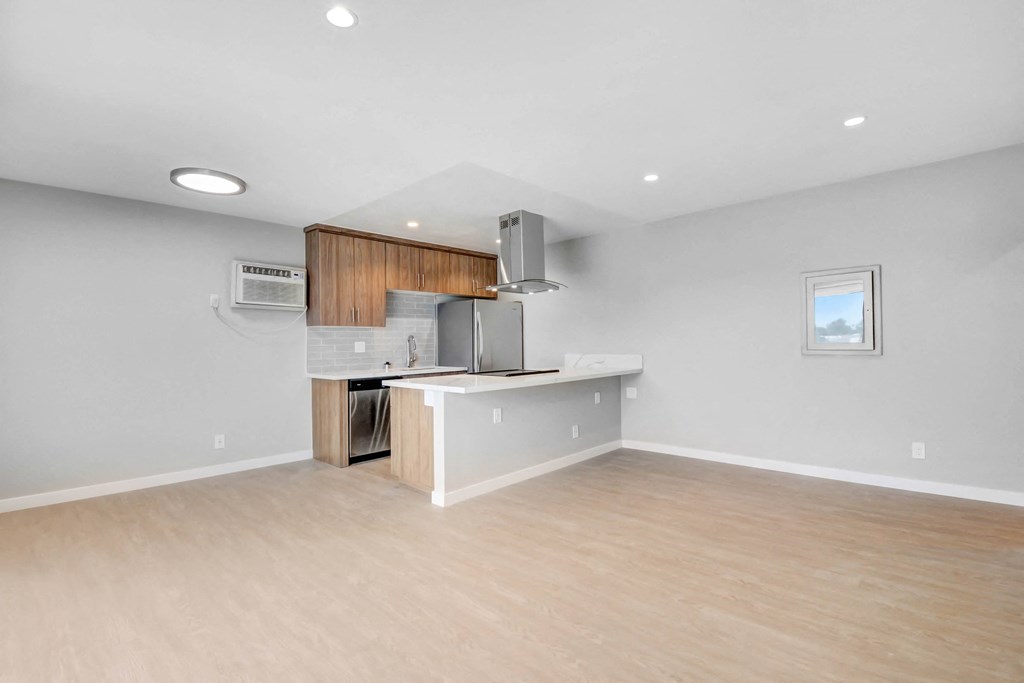 an empty living room and kitchen with wood floors and white walls