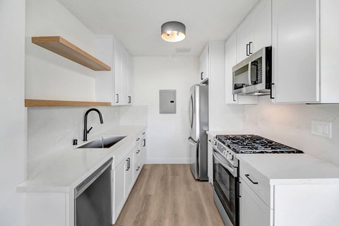A modern kitchen with white cabinets and a wooden shelf.