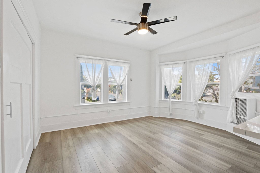 an empty living room with a ceiling fan and three windows