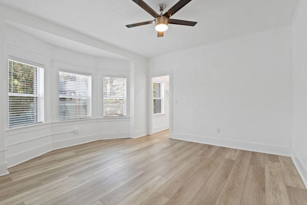 an empty living room with a ceiling fan and windows