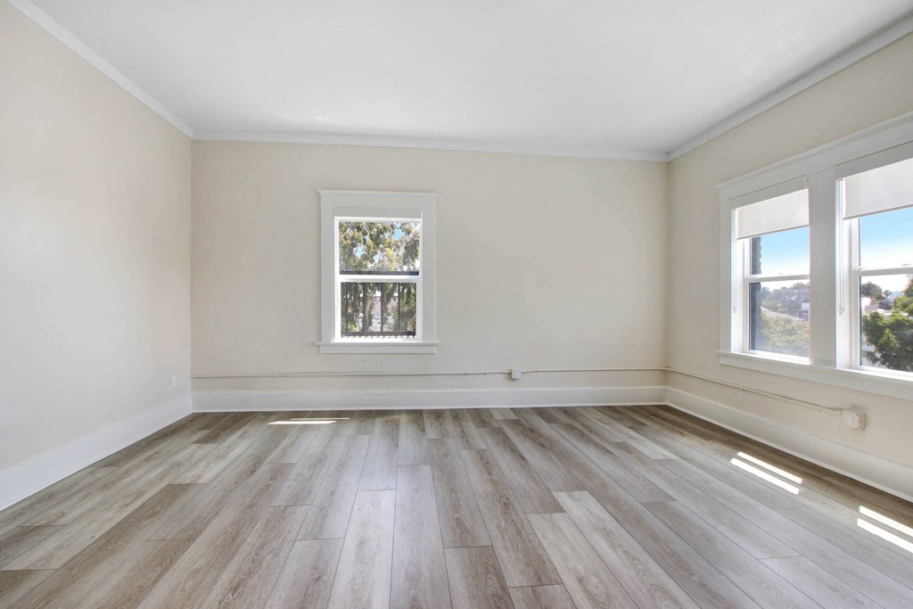 an empty room with wooden floors and two windows
