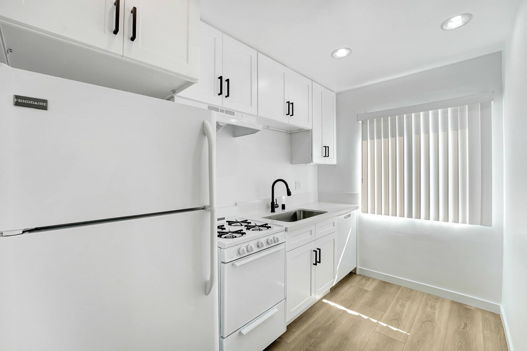 A white kitchen with a refrigerator, sink, and cabinets.
