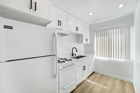 A white kitchen with a refrigerator, sink, and cabinets.