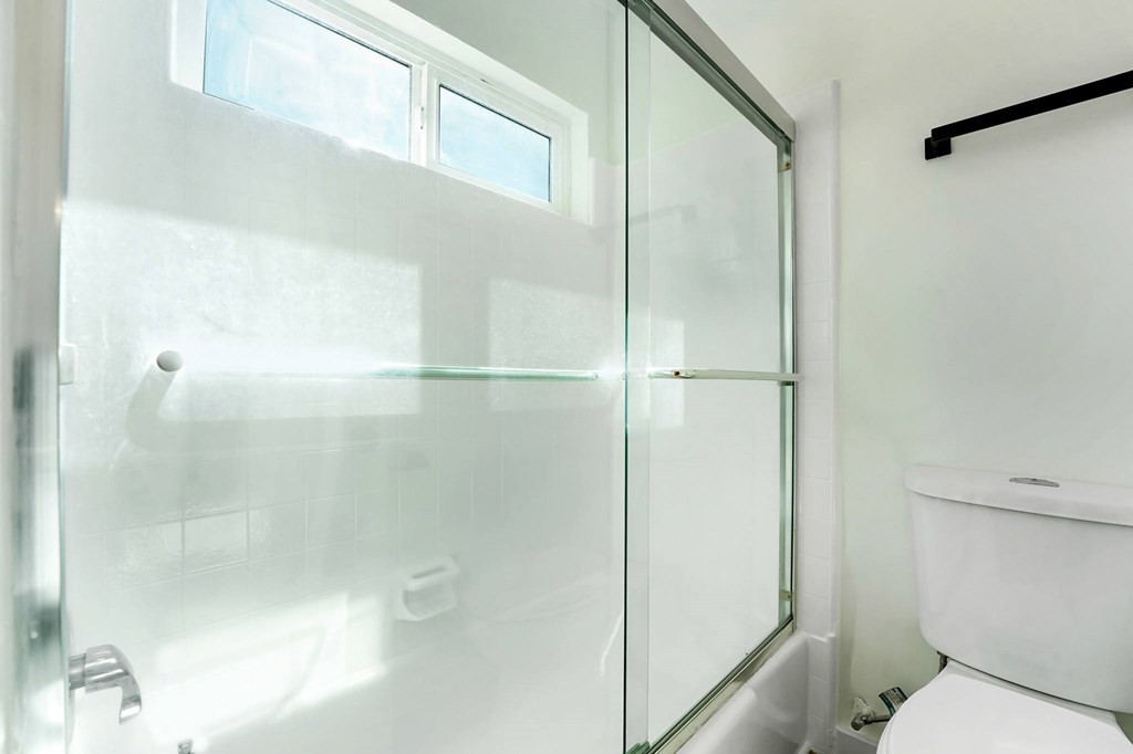 A white bathroom with a glass shower door and a white toilet.