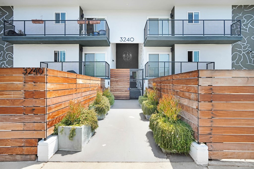 A modern building with a black door and windows, surrounded by wooden fences and plants.