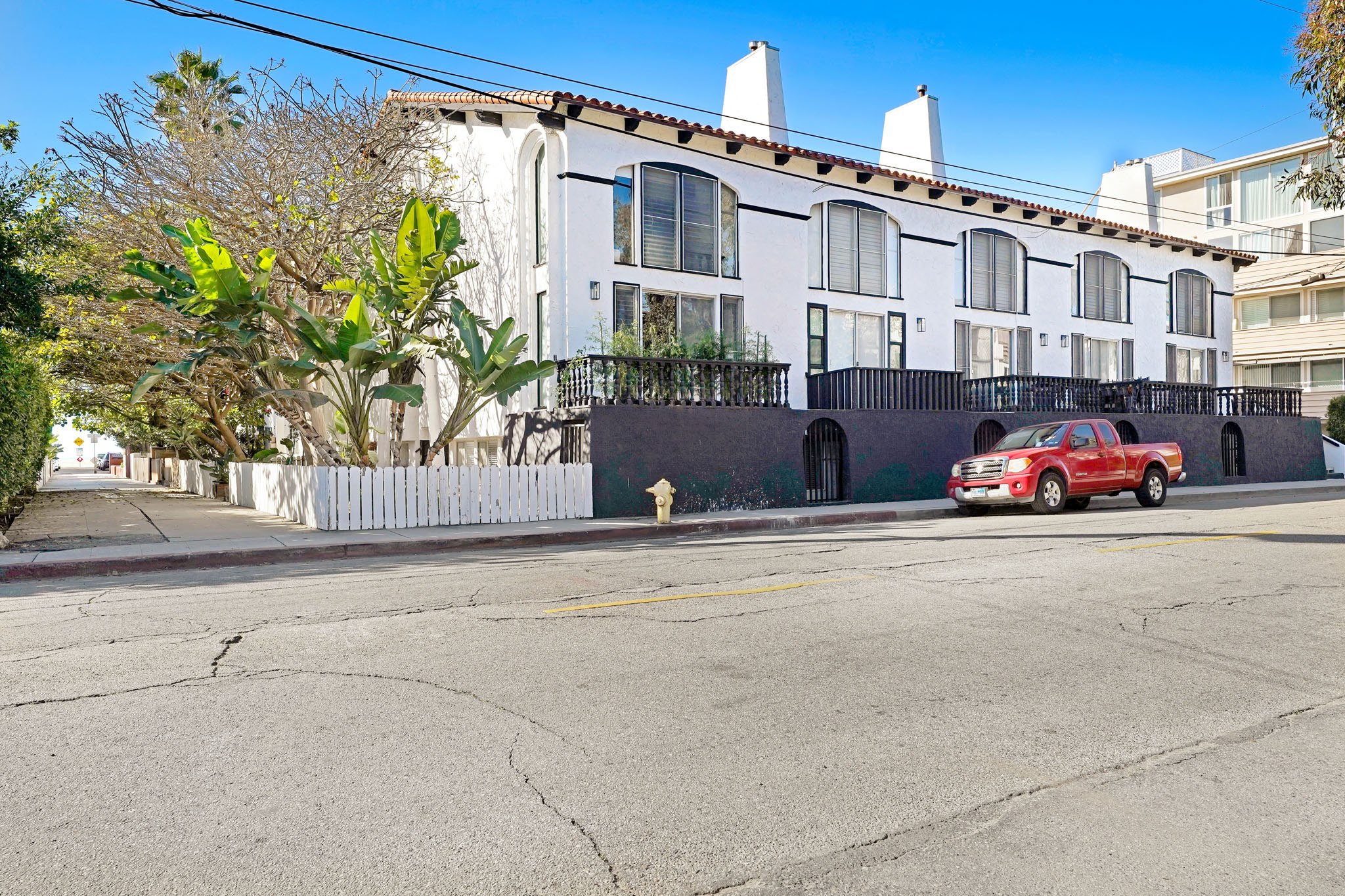 A red car is parked on the side of a street in front of a white building.