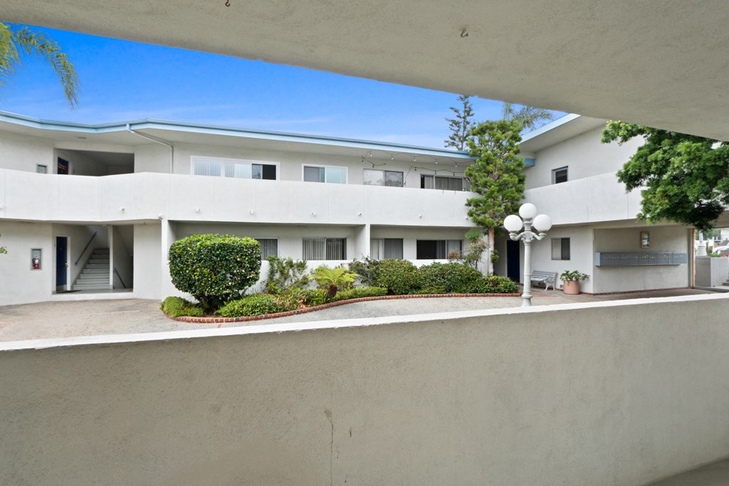 a view of a white building from a balcony with trees and bushes