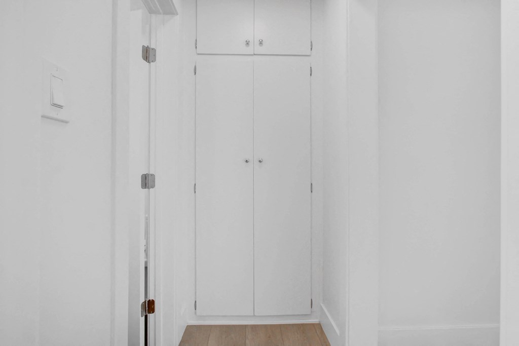a long white hallway with two white closets and a wood floor