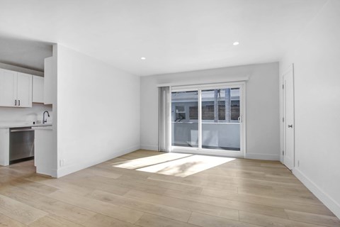 A spacious room with wooden flooring and a large window with blinds.