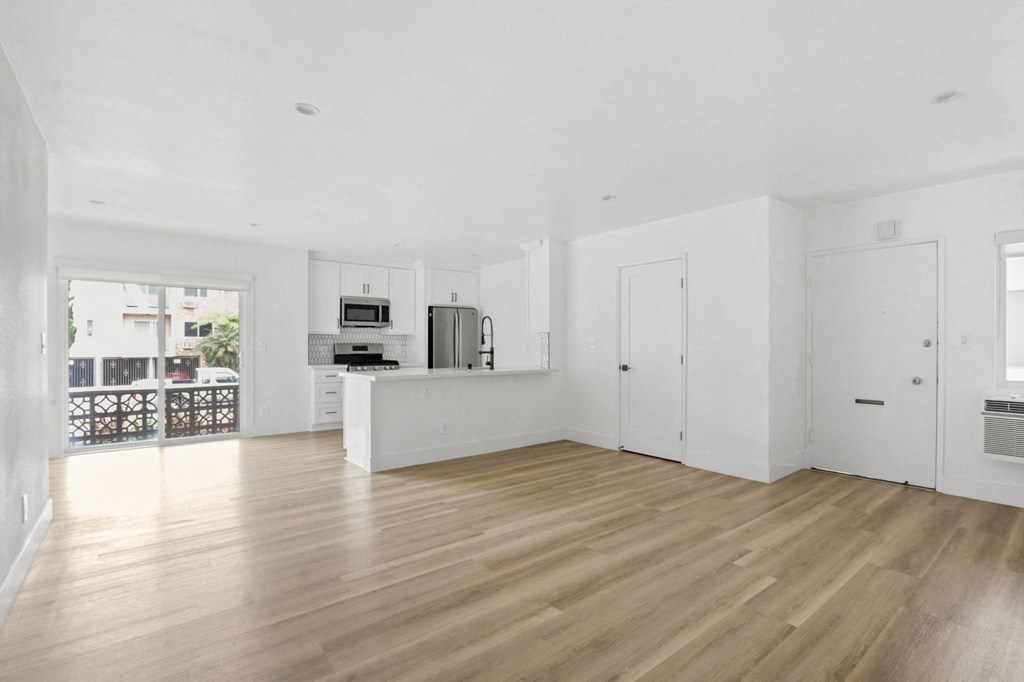 the living room and kitchen of an apartment with white walls and wood floors