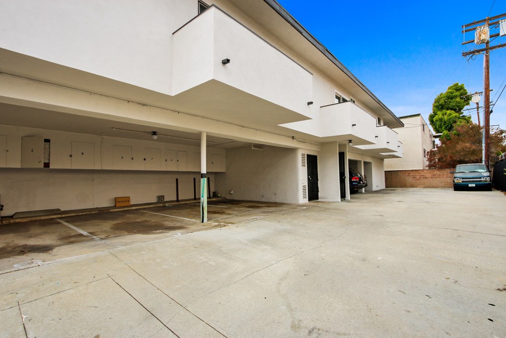the parking lot of a white building with a car parked under it