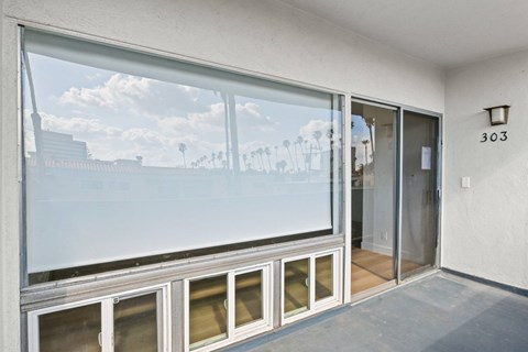 A room with a large window showing a view of a building and palm trees outside.