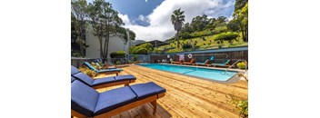 A pool with a wooden deck and lounge chairs.