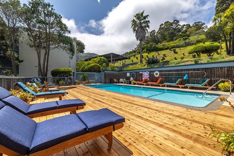 A pool with a wooden deck and lounge chairs.