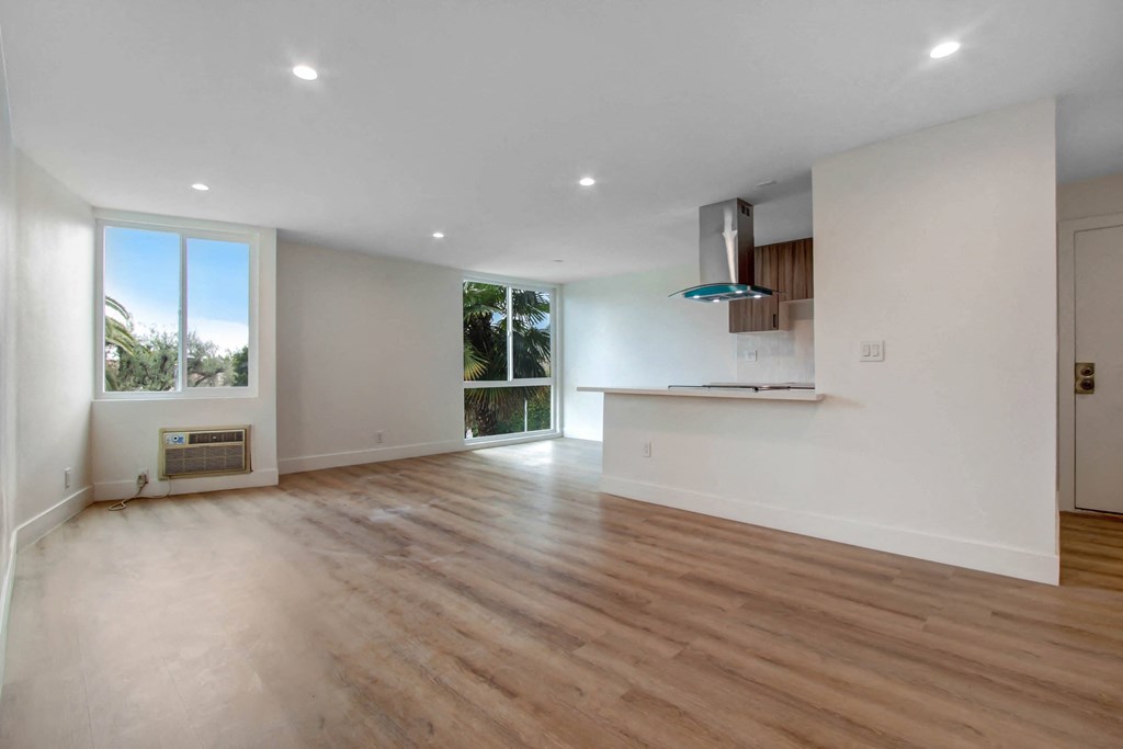 an empty living room with a kitchen and a large window