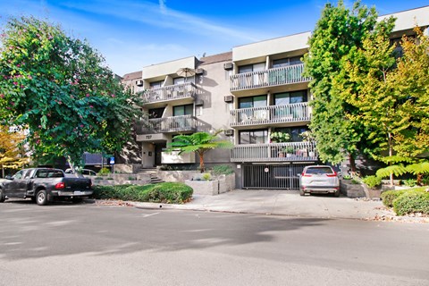A black car is parked on the left side of a street in front of a building with a balcony.