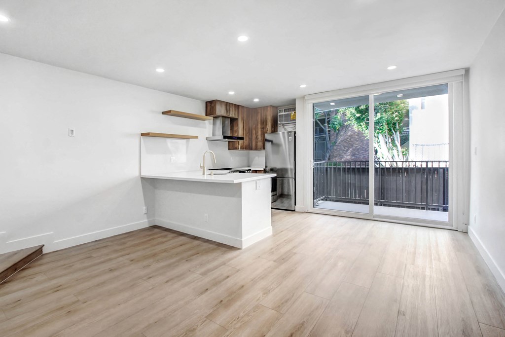 an empty living room with a kitchen and a sliding glass door