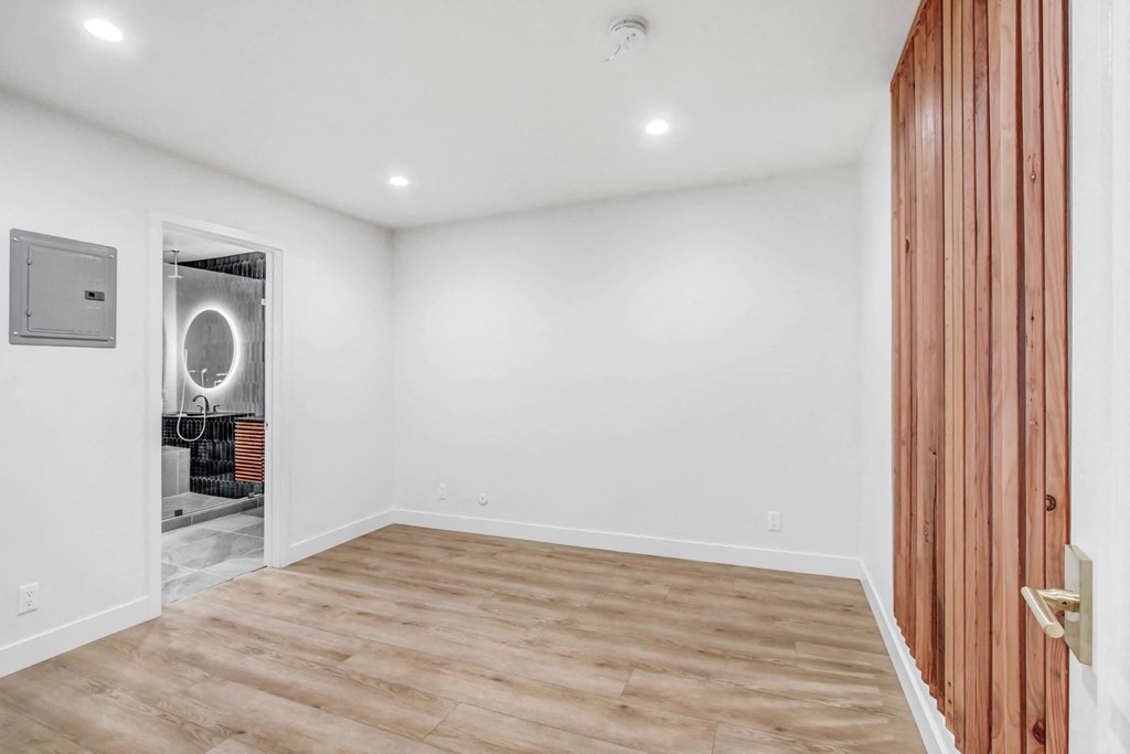 a room with white walls and a wooden floor and a door to a bathroom