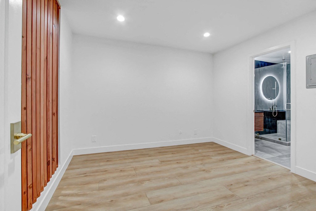 a room with white walls and a wooden floor and a door to a bathroom