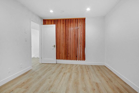 a living room with white walls and wood floors and a wooden curtain on the wall