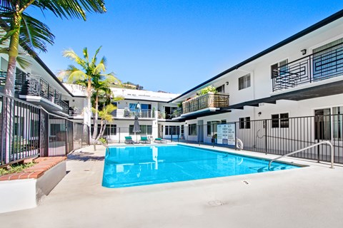 A swimming pool in a sunny courtyard surrounded by buildings.