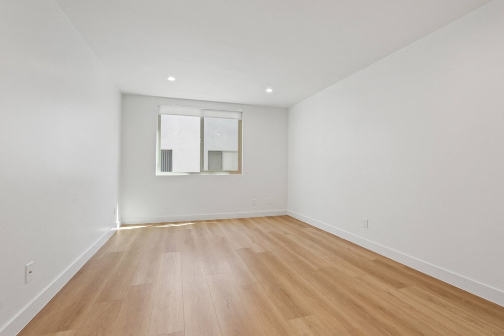 a living room with white walls and wooden floors and a window