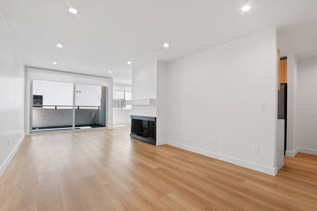 an empty living room with a fireplace and a kitchen