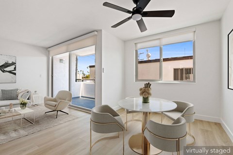 A living room with a white table and chairs, a ceiling fan, and a view of the outdoors through the windows.