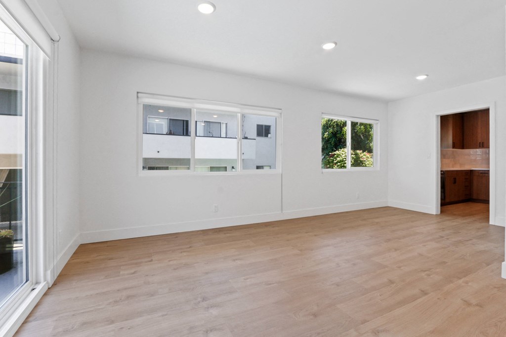 a living room with white walls and a wooden floor and windows