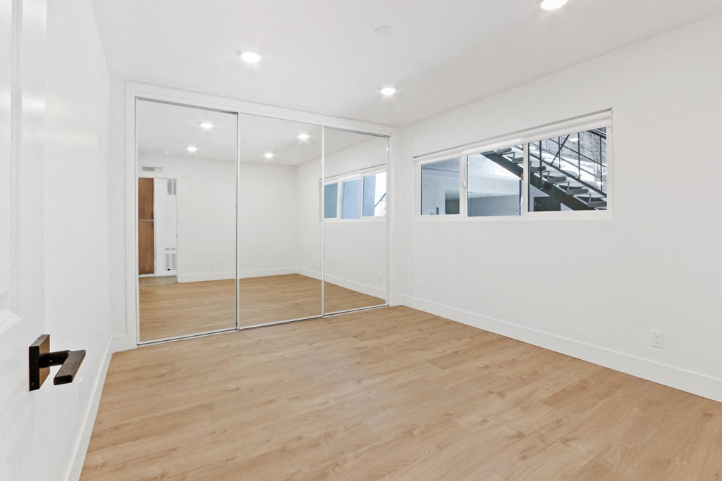 a living room with a hardwood floor and white walls with mirrors and a door