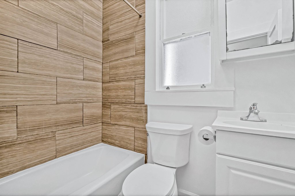 A white toilet sits next to a white bathtub in a bathroom with wooden wall tiles.