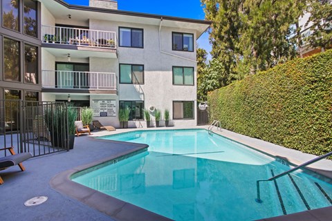 A swimming pool in front of a white building with a balcony.