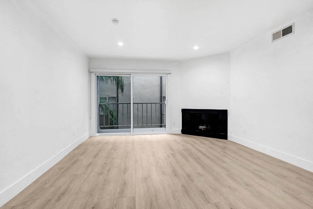 a living room with white walls and a sliding glass door to a balcony