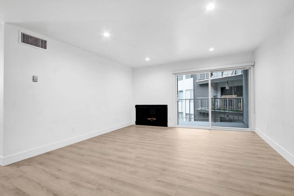 a living room with white walls and a sliding glass door to a balcony
