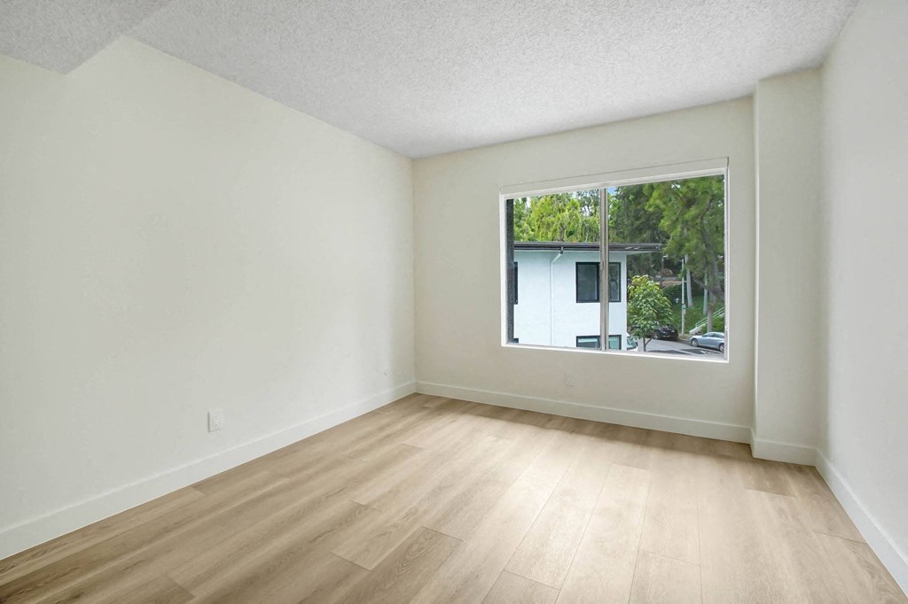 an empty living room with a large window and wooden floors
