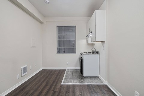 A kitchen area with a white fridge and a window with blinds.
