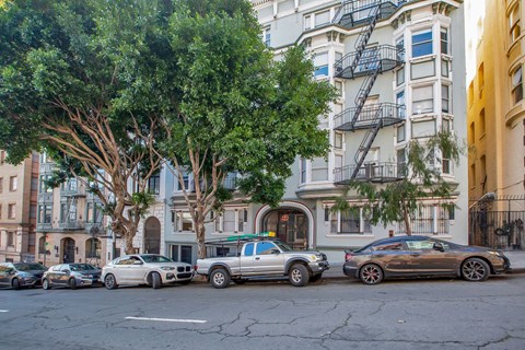 Cars parked on a street in front of a building with a tree.