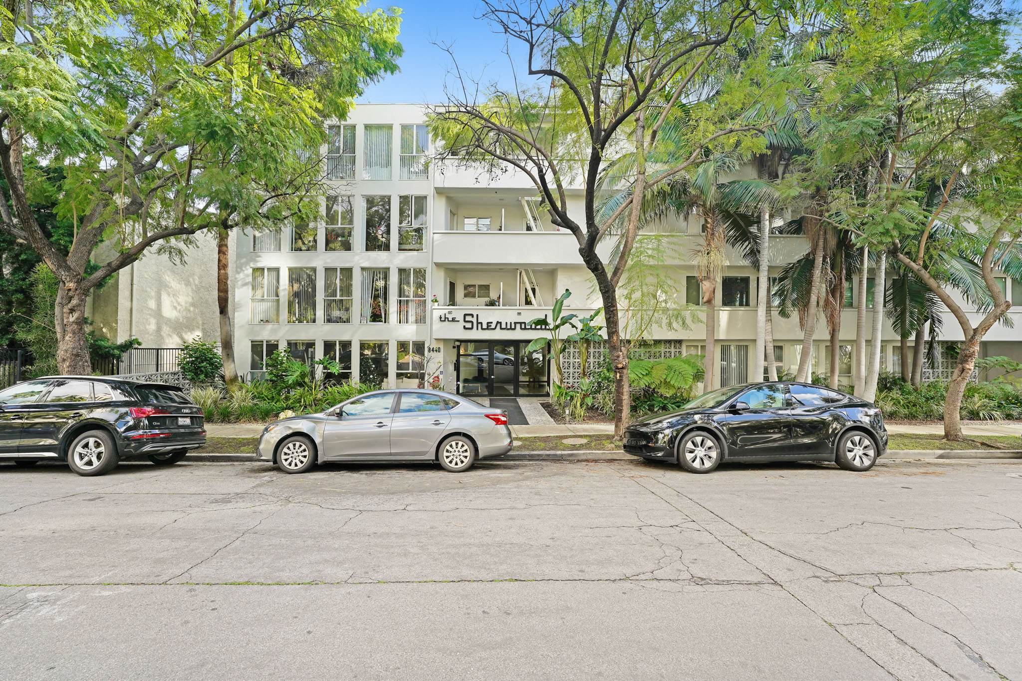 Three cars are parked in front of a white building with the name Shearman on it.