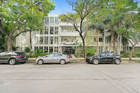 Three cars are parked in front of a white building with the name Shearman on it.