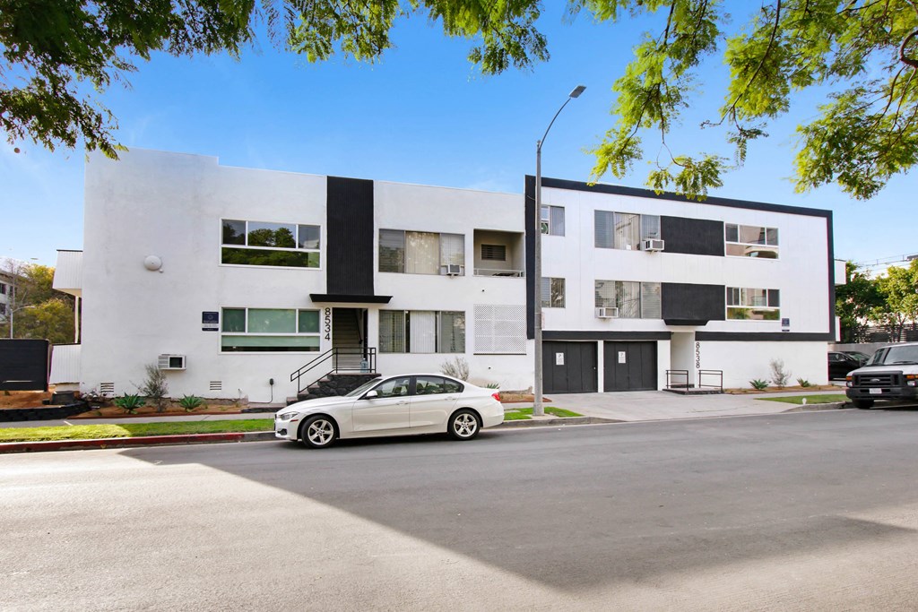 a white car parked in front of a white and black apartment building