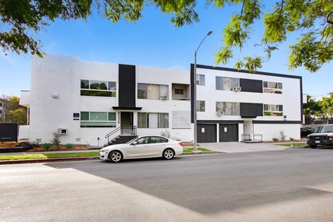 A white car is parked in front of a modern two-story building.