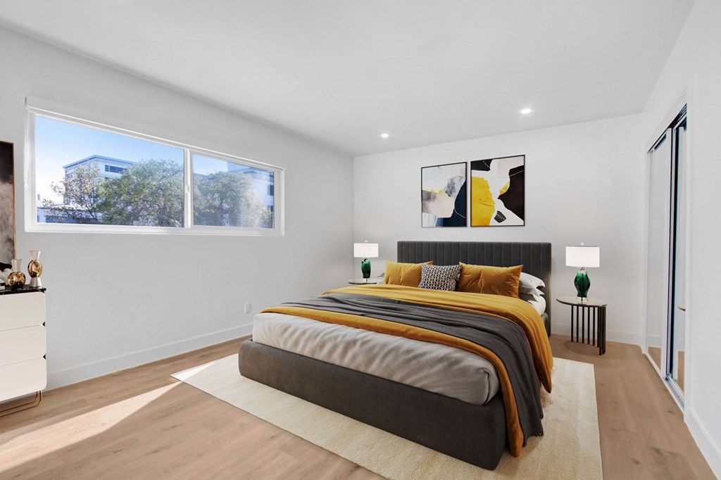 A bedroom with a large bed and a view of a building outside the window.