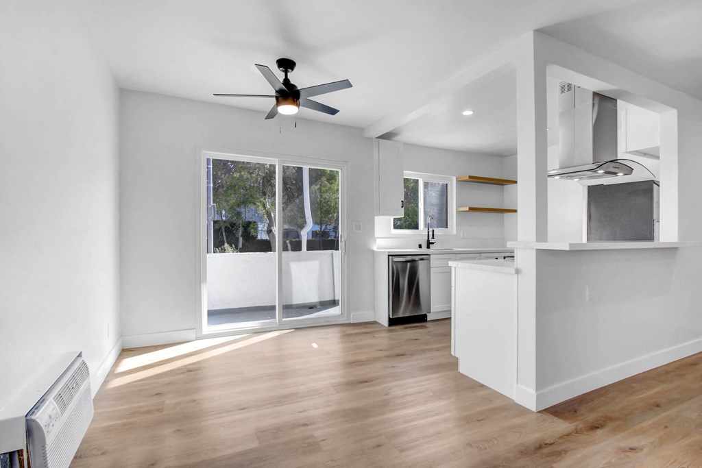 an empty living room with a ceiling fan and a door to a kitchen