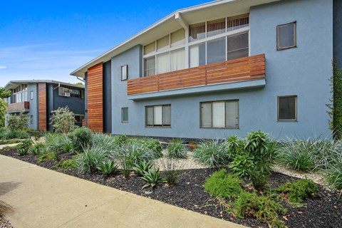 A modern two-story building with a balcony and a garden in front.