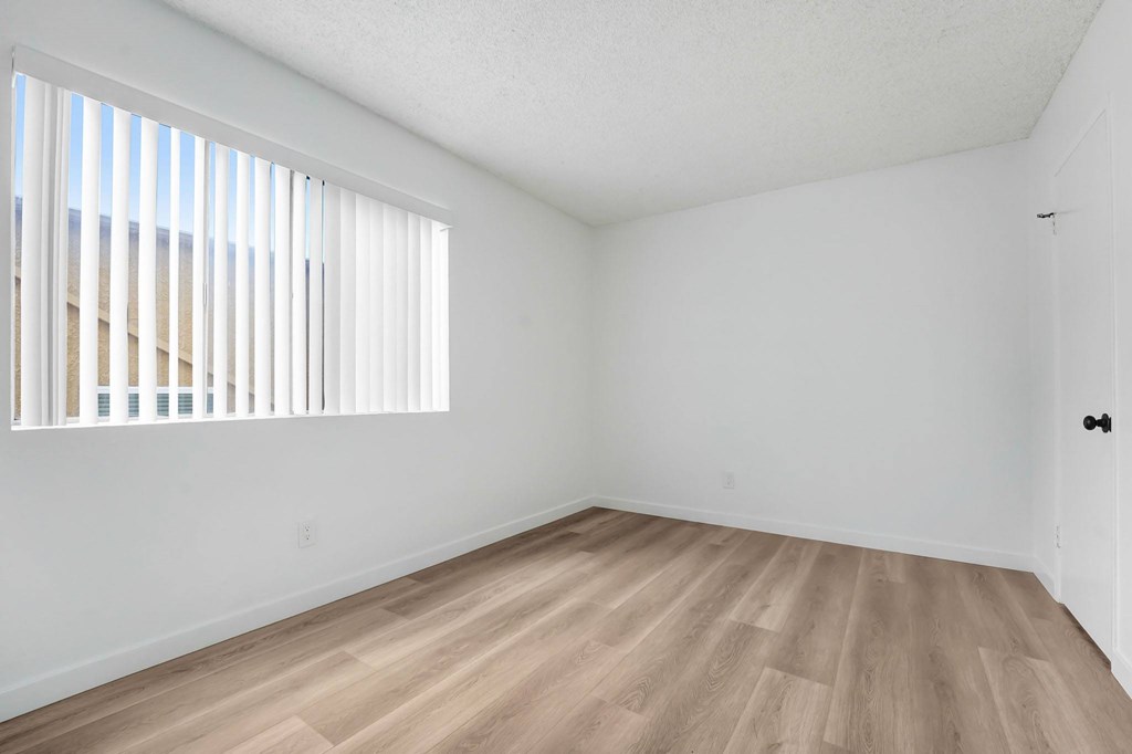 A room with wooden flooring and a window with blinds.