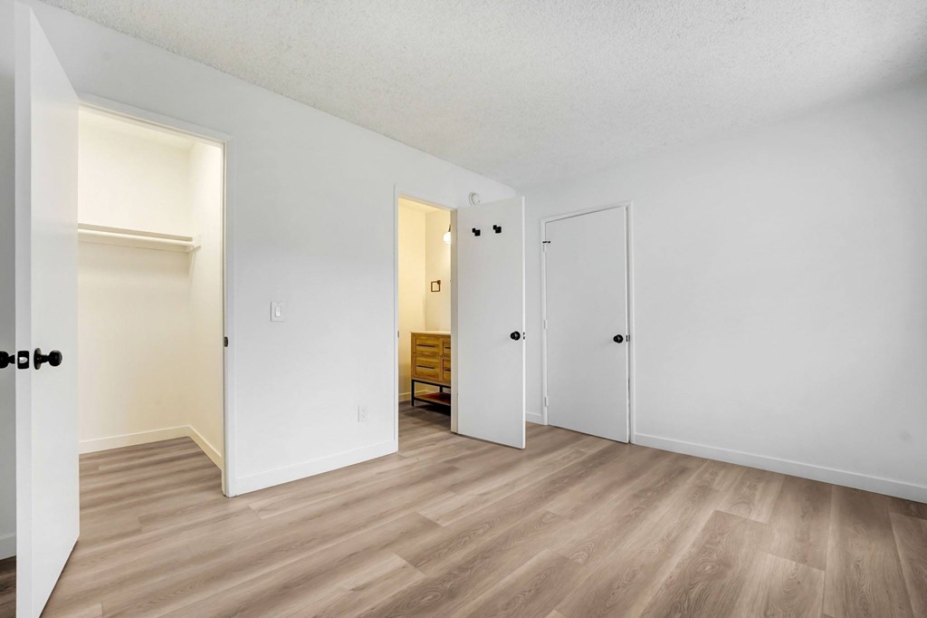 A room with white walls and wooden flooring with three doors.