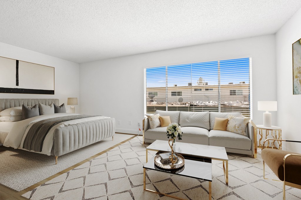 A well-lit, modern bedroom with a large bed, a couch, a coffee table, and a view of a parking lot outside.
